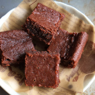 photo of paleo vegan almond flour brownies on parchment paper, white plate, grey background from Flash Fiction Kitchen