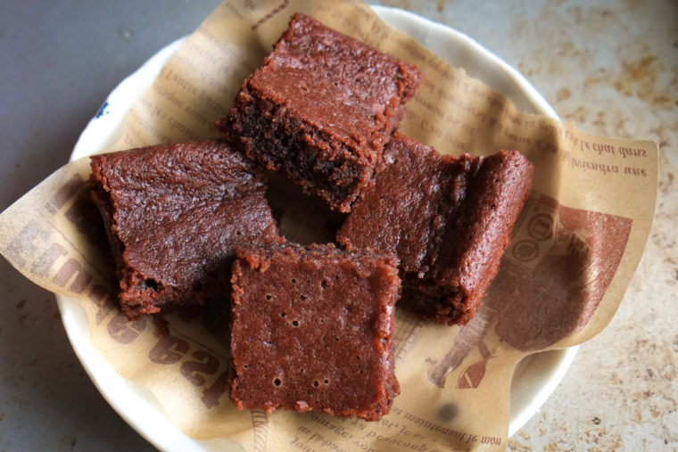 photo of paleo vegan almond flour brownies on parchment paper, white plate, grey background from Flash Fiction Kitchen